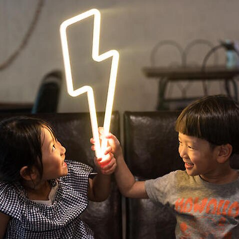 Two small children holding a lightning bolt shaped neon light