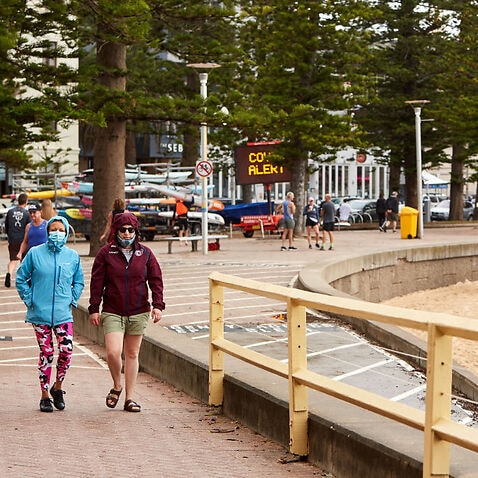 People with masks walk along the Manly beachfront.