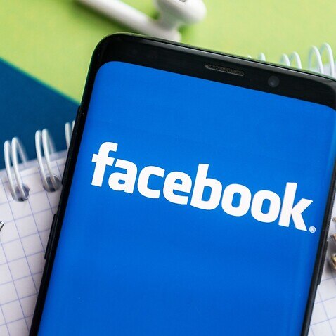 In this photo illustration, a Facebook logo seen displayed on a smartphone with a pen, key, book and headsets in the background