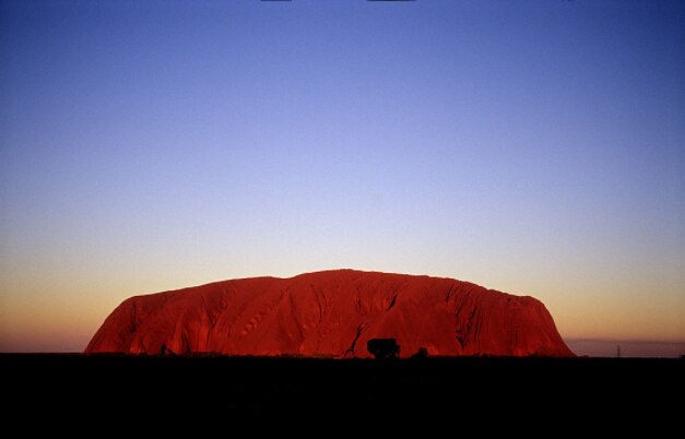 The red rock face of Uluru at sun set, the sacred home for thousands of years of the Yankunytjatjara and Pitjantjatjara people in the central Australian desert.