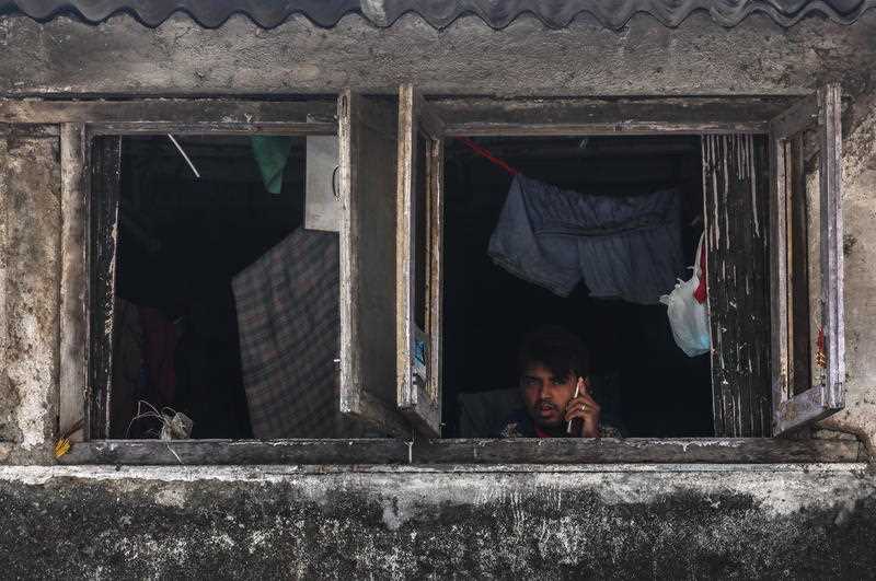 An Indian man looks out from the window of his room in the Dharavi slums
