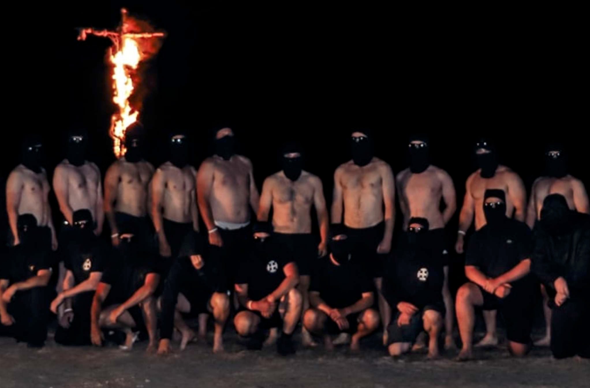 A group of white men stand under a burning cross at Gariwerd, Victoria.