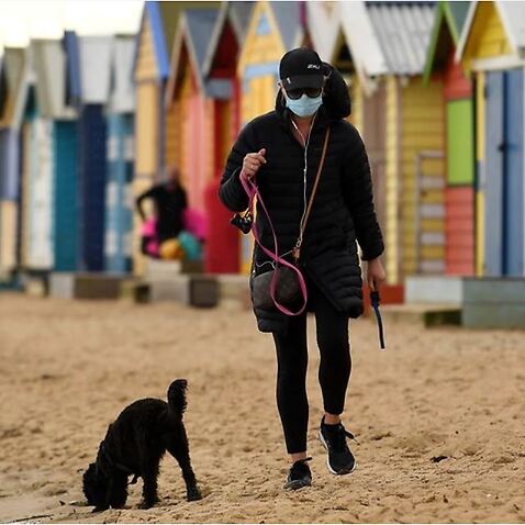 A person wearing a face mask is seen walking their dog along Brighton beach in Melbourne during the Stage Four lockdown. 