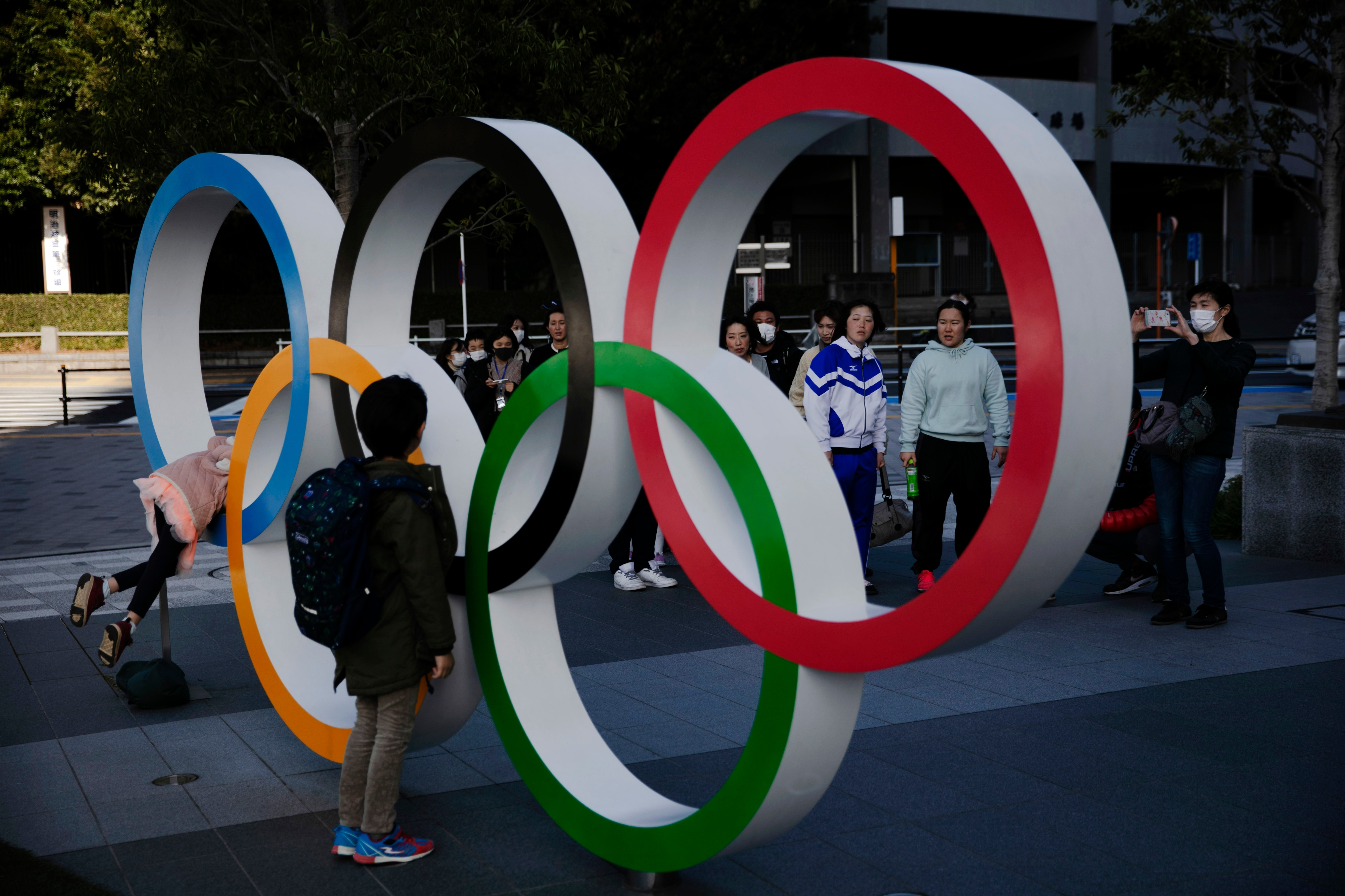 People wait in line to take pictures with the Olympic rings near the New National Stadium in Tokyo.