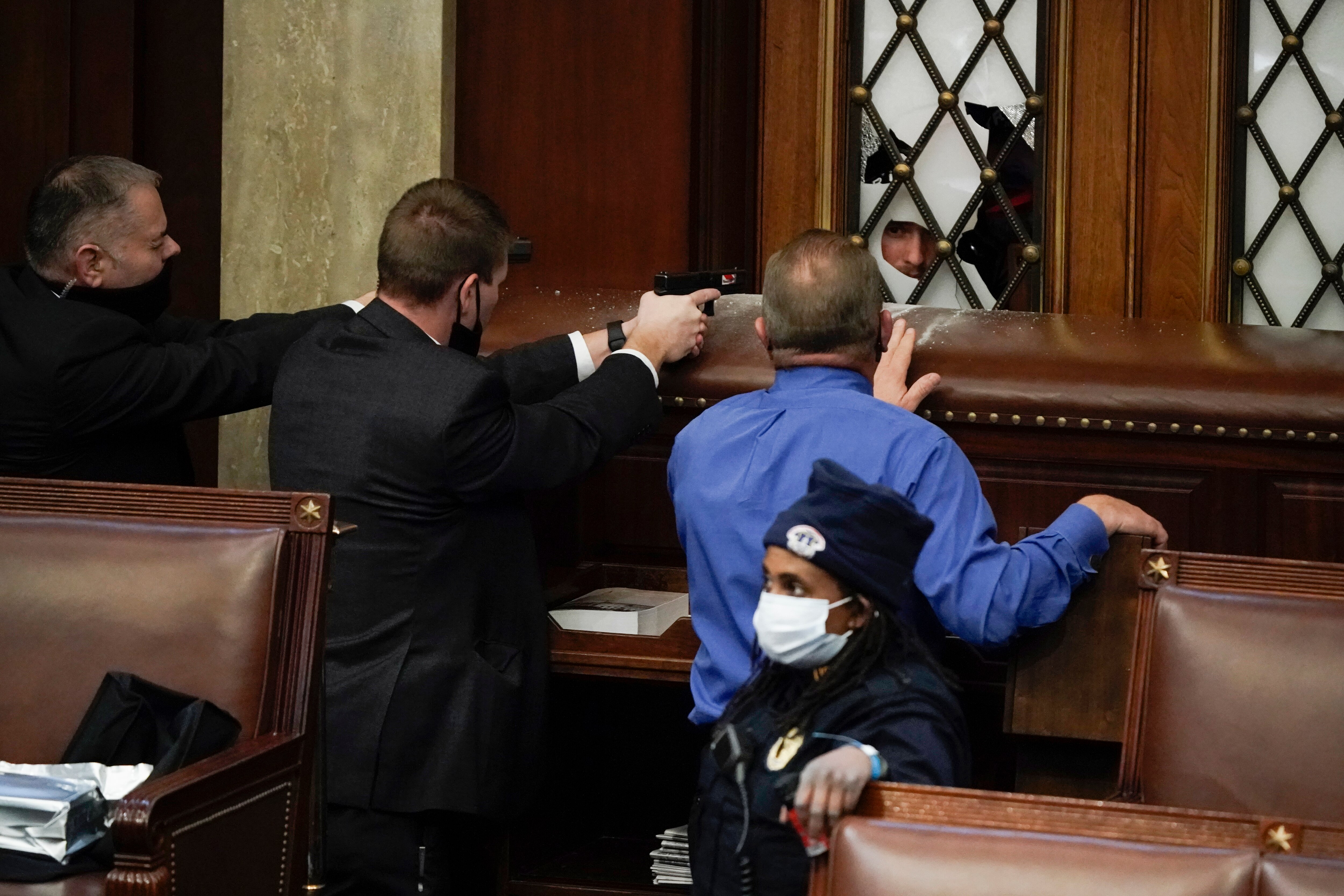 Police with guns drawn watch as protesters try to break into the House Chamber at the U.S. Capitol building. 