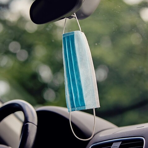 Face protective mask hanging at rear view mirror in car