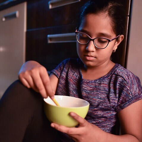 Girl eating from bowl while sitting on kitchen floor