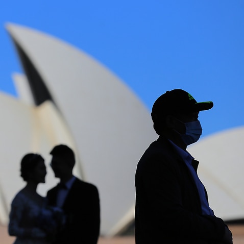 People wear face masks in front of the Sydney Opera House in Sydney.