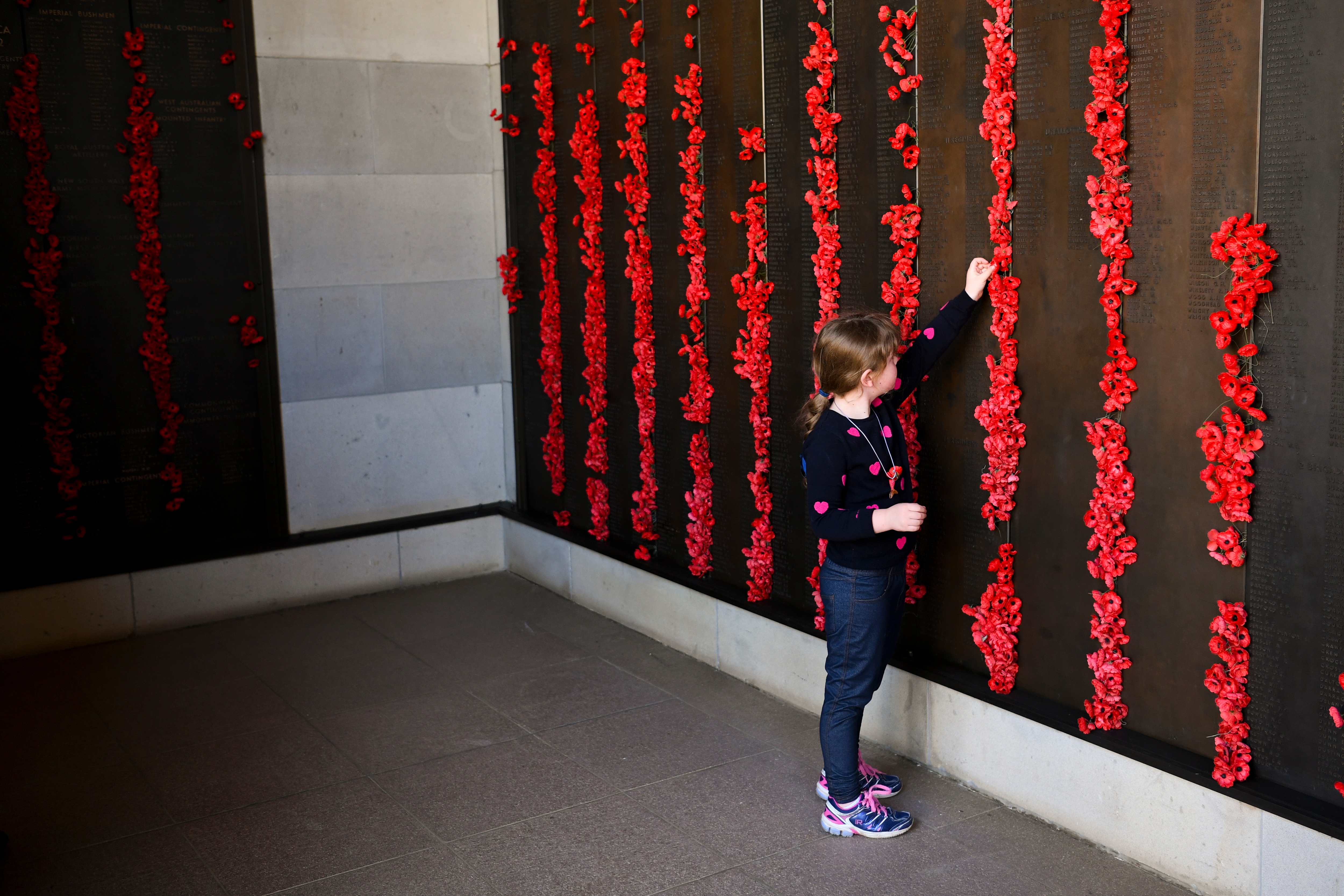 A young girl places a poppy on the Roll of Honour after the Anzac Day National Service at the Australian War Memorial in Canberra, Sunday, April 25, 2021. (AAP Image/Lukas Coch) NO ARCHIVING