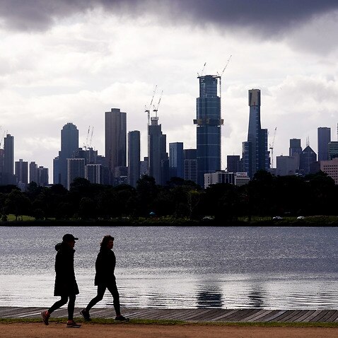 People walk around Albert Park Lake as storm clouds hover over the city skyline in Melbourne.