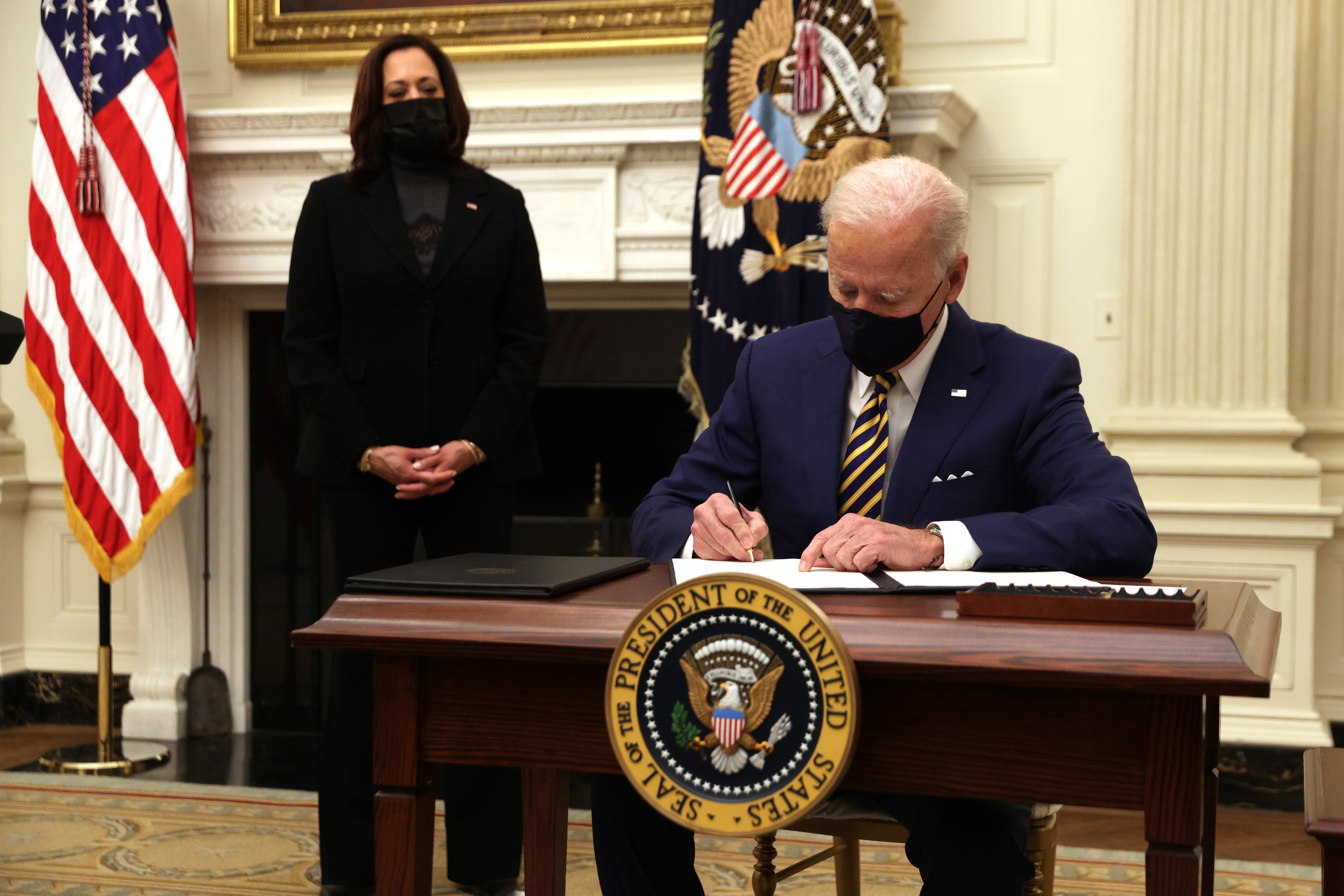 US President Joe Biden signs an executive order as Vice President Kamala Harris watches at the White House on January 22, 2021.
