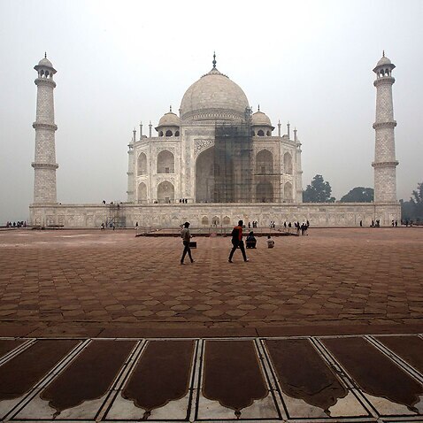 Tourists walk around Taj Mahal as workers clean the monument in Agra, India.