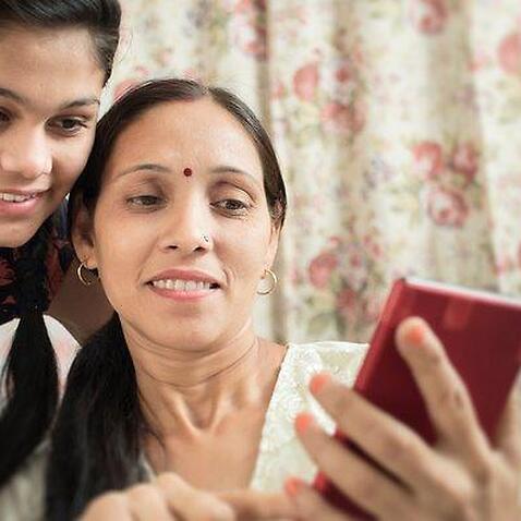 Mother and daughter using phablet together in domestic room.