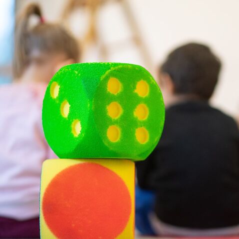 : Two cubes stand in a day care center in front of children sitting in a circle. 
