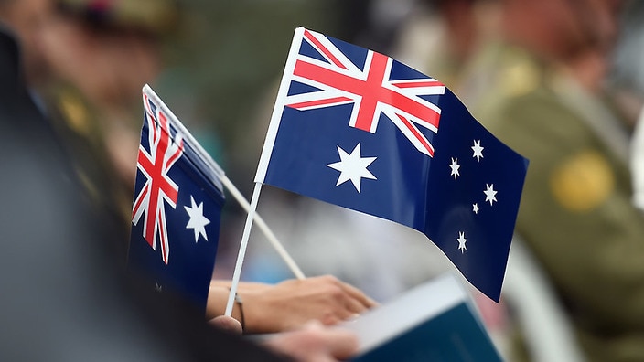 Members of the public hold flags at an Australia Day Citizenship Ceremony and Flag Raising event in Canberra