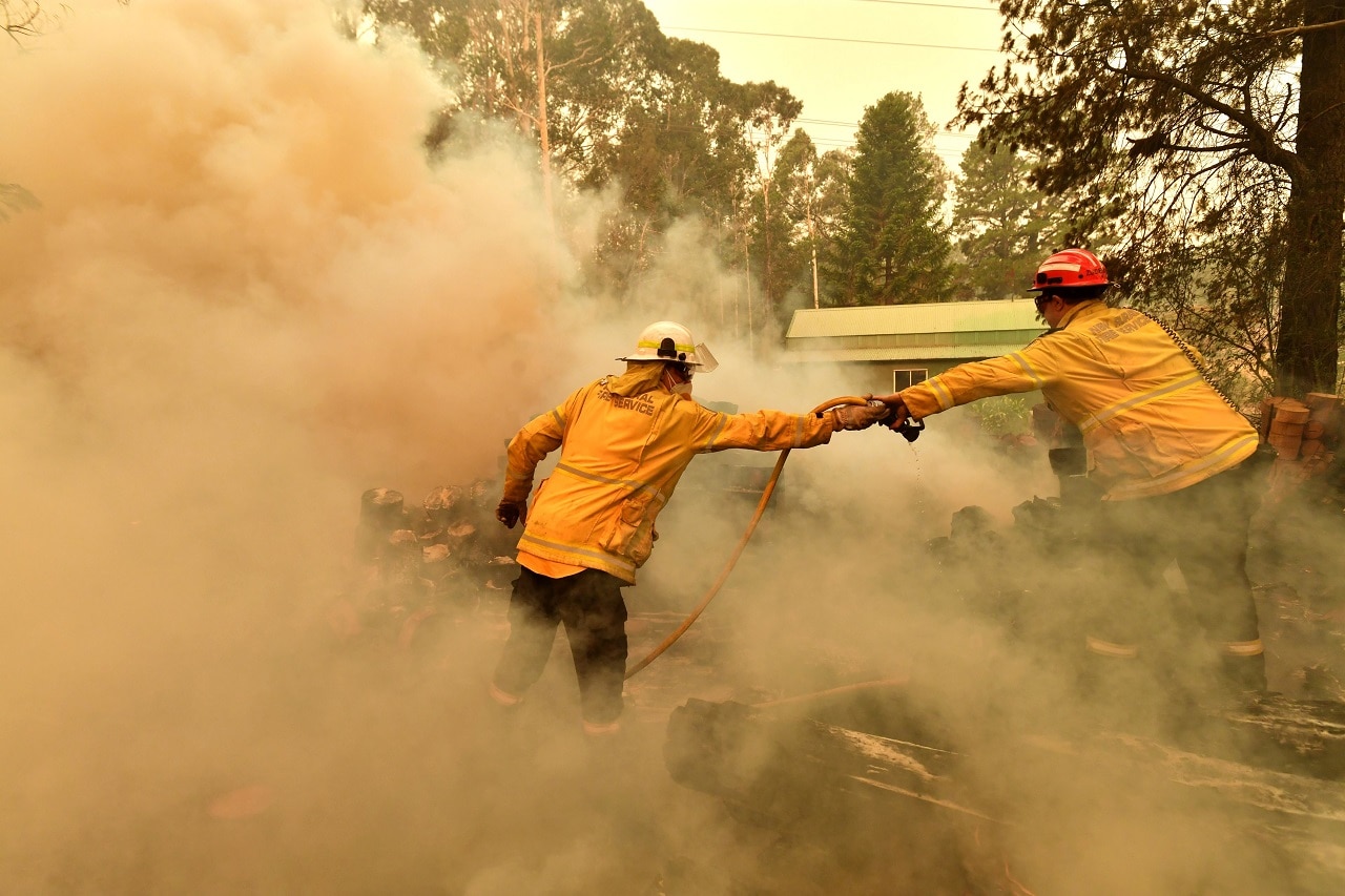 Firefighters hose down a burning woodpile during a bushfire in Werombi, south-west of Sydney. Firefighters hose down a burning woodpile during a bushfire in Werombi, south-west of Sydney.