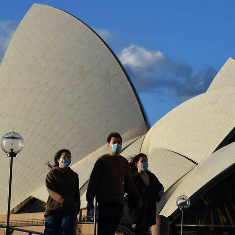 Pedestrians wearing masks walk past the Sydney Opera House.