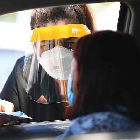 A woman wearing a face shield and face mask gives a rapid antigen test kit to a woman in a car in Melbourne.