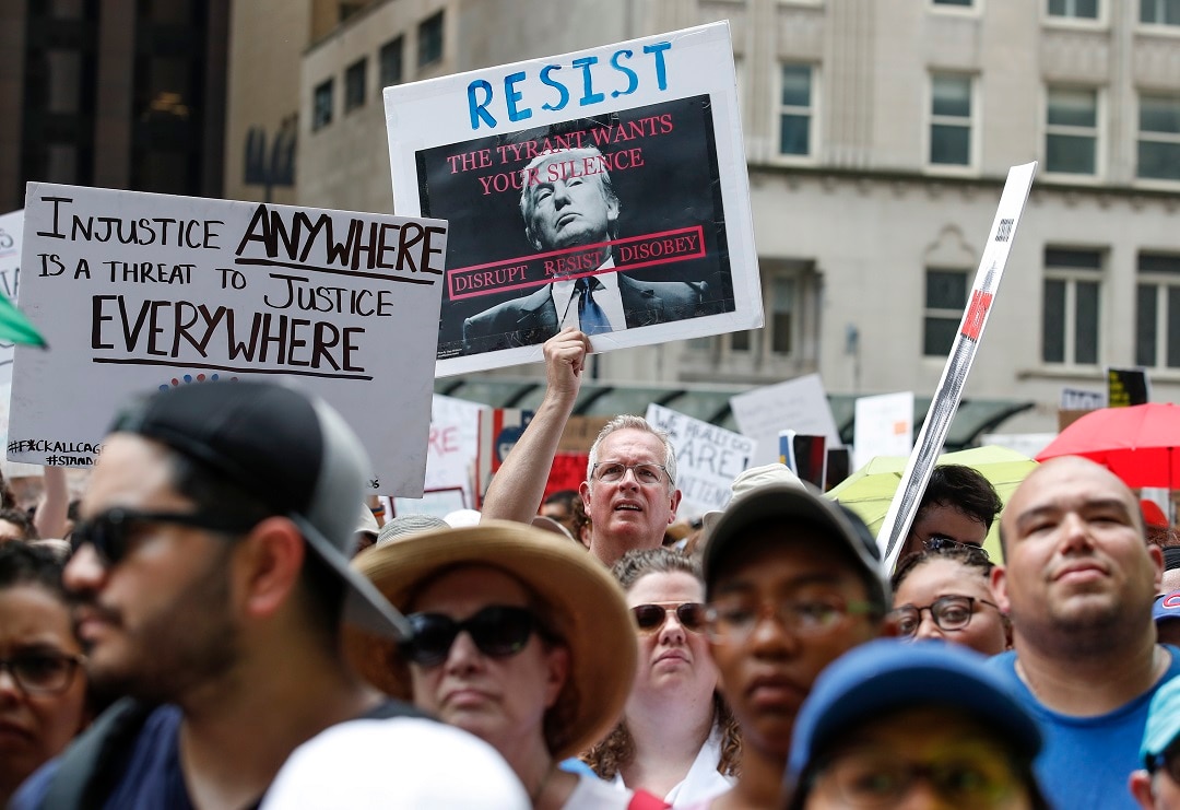 A male binds a pointer reading Resist during a proof opposite Donald Trump's immigration policies.