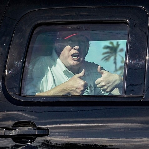 President Donald Trump gives two thumbs up to supporters on his way to the Mar-a-Lago estate after spending the morning at Trump International Golf Club.