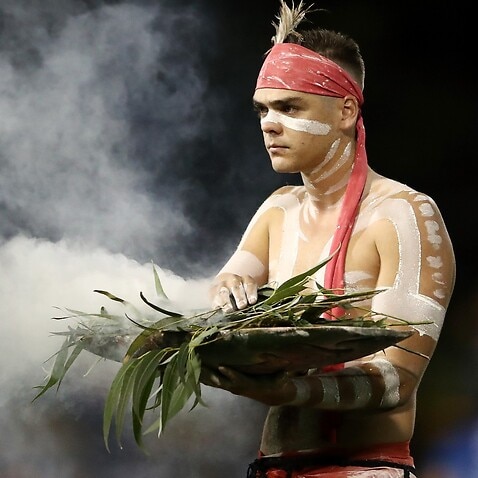 An Indigenous performer participates in a smoking ceremony