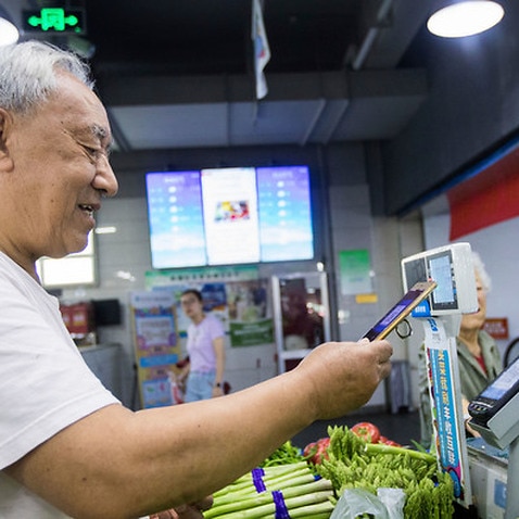 A citizen scans a QR code via mobile payment service Alipay of Alibaba Group on his smartphone to pay for vegetables at a market in Hangzhou city