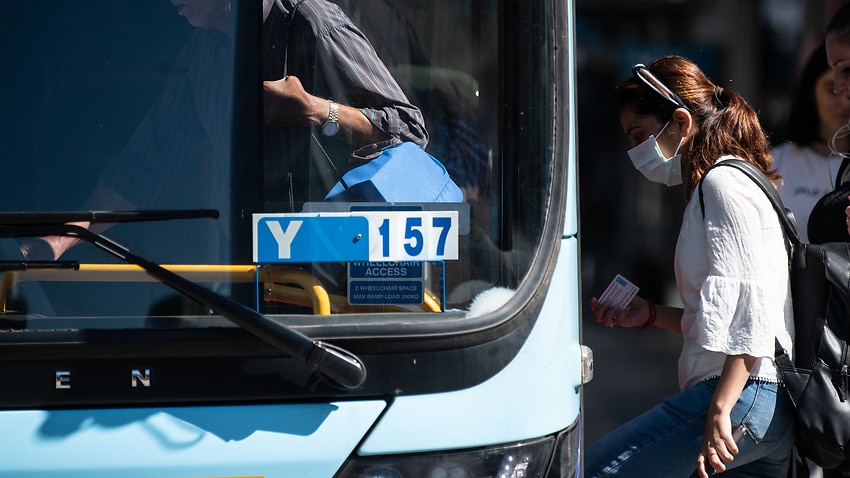 A woman wearing a protective face mask boards a bus in Sydney, Friday, 13 March, 2020.