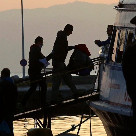 A migrant is escorted into a ferry in the port of Mytilene