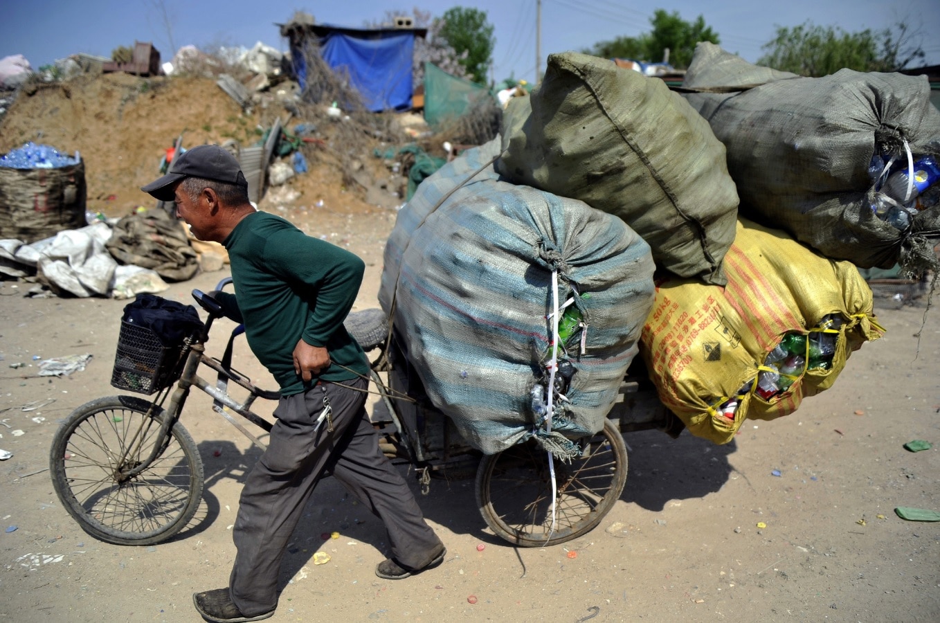 A man transports a tricycle load of many waste plastic bottles for recycling at a reclamation depot in Qingdao city