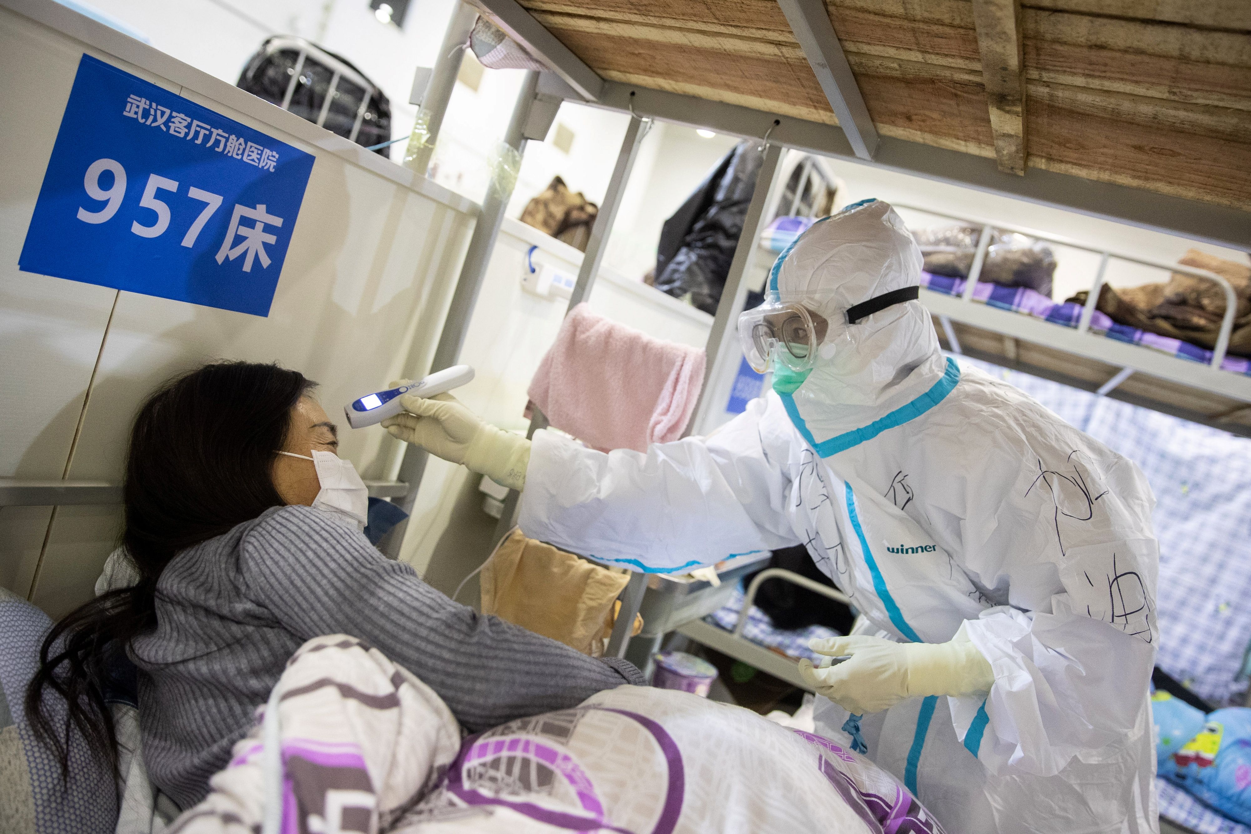 A medic working inside a makeshift hospital in Wuhan checks the temperature of a patient who has displayed mild symptoms consistent with coronavirus.