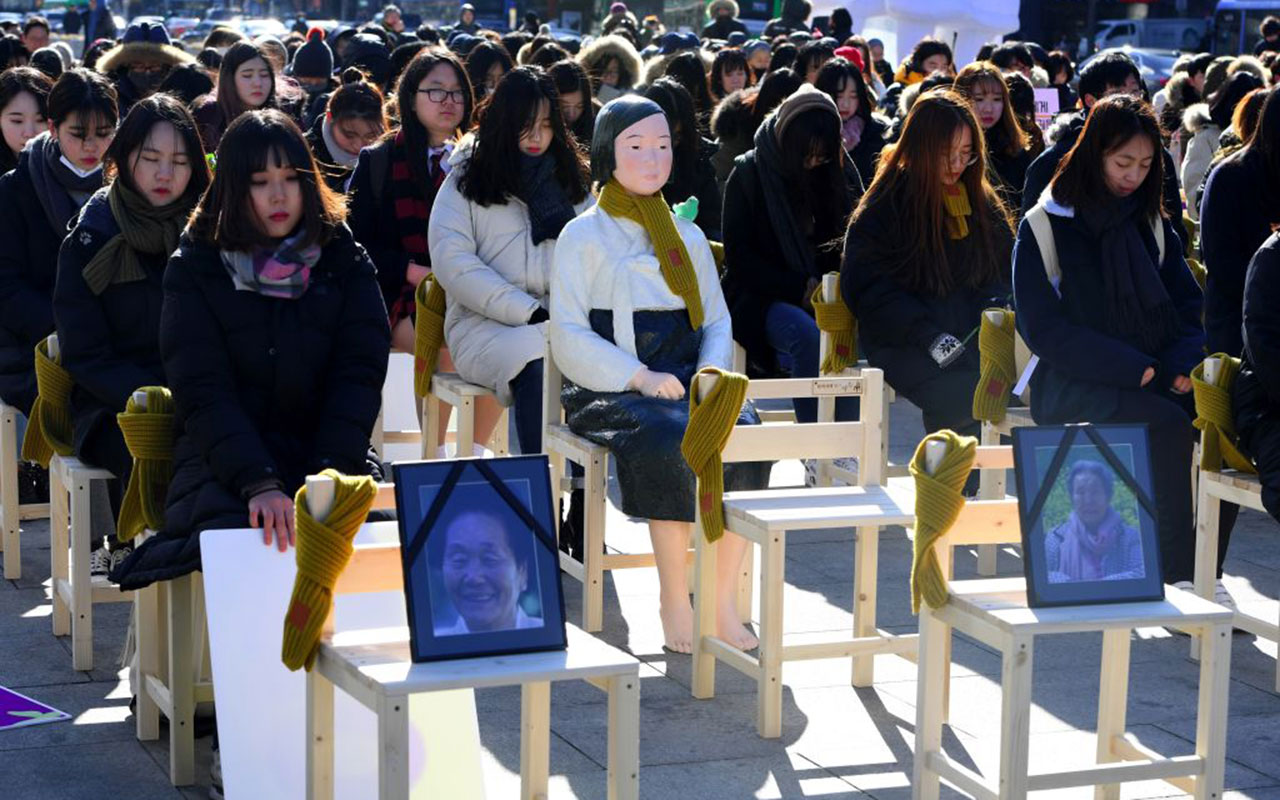 People sit around a statue of a 'comfort woman' (C) during an installation of empty chairs.