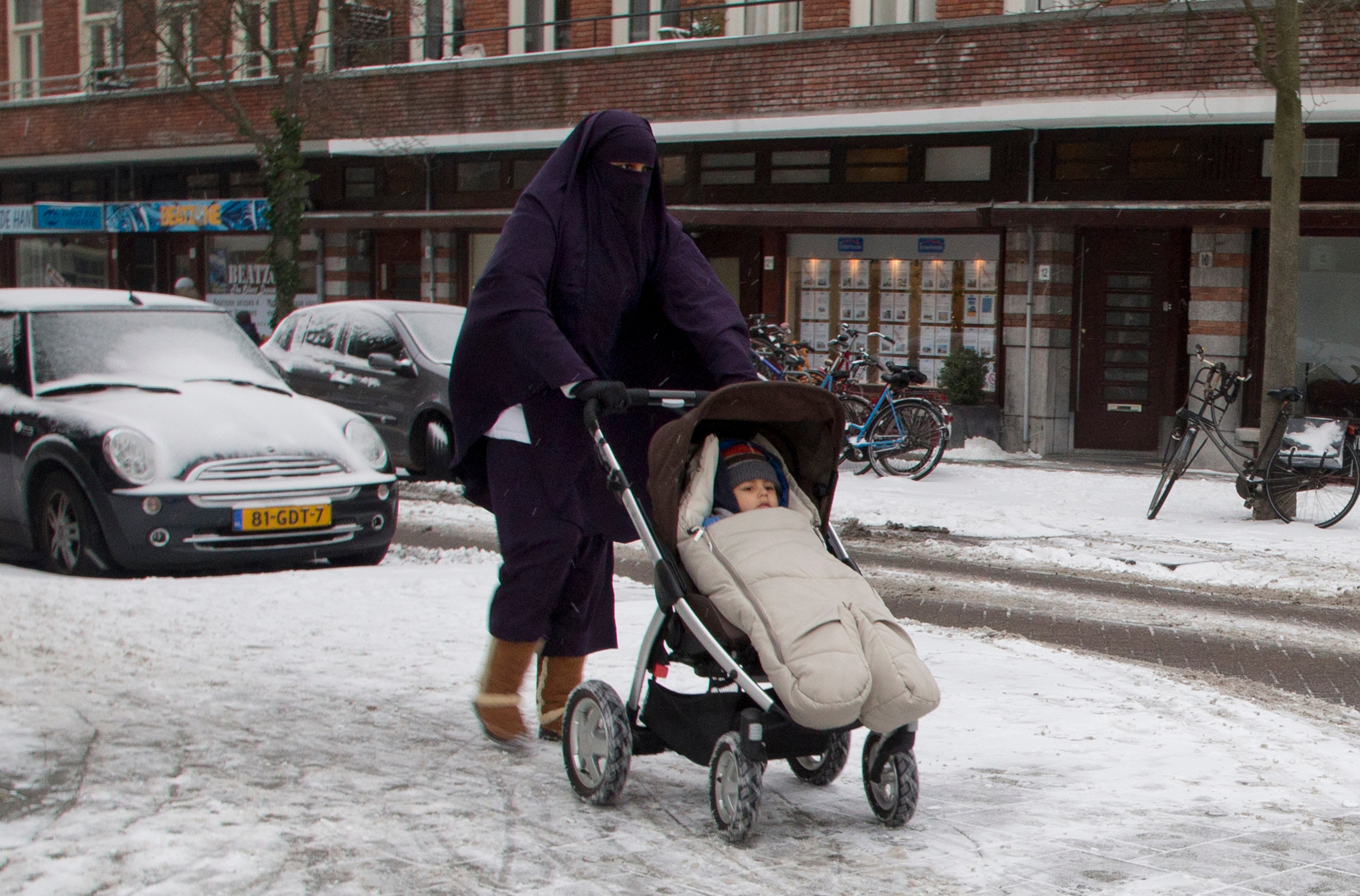A woman wearing a niqab pushes a baby stroller on snow-covered streets in Amsterdam.