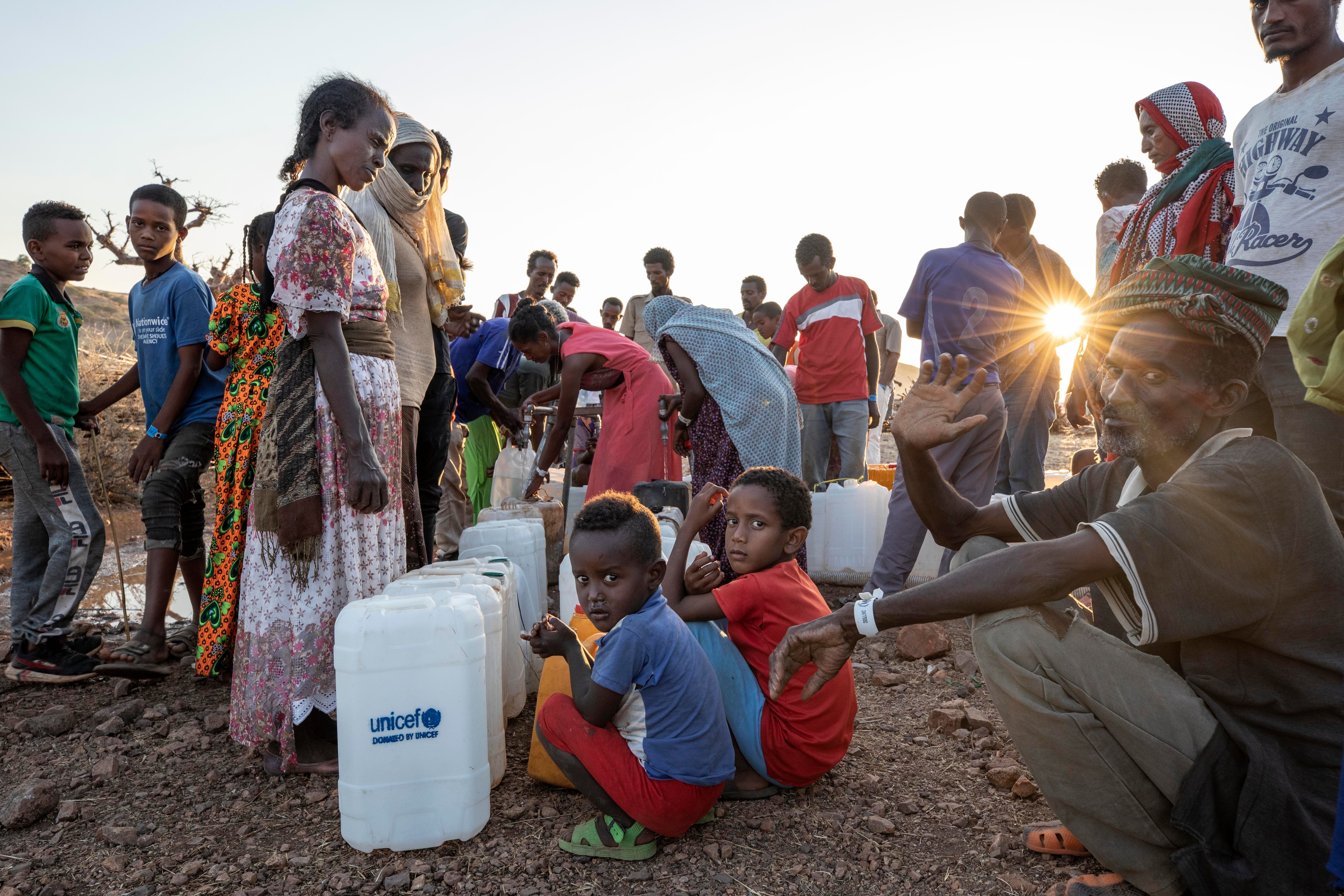 Women and men who fled the conflict in Ethiopia's Tigray region, wait to pour water into gallons, at Umm Rakouba refugee camp in eastern Sudan on 27 November.