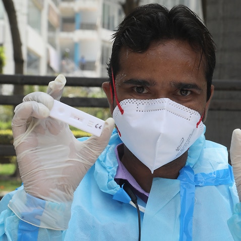 A healthcare worker wearing personal protective equipment (PPE) holds test sticks after collecting nasal swab sample for a Covid-19 rapid antigen test.