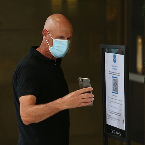 A man wearing a face mask scans a COVID-19 check in QR code in Sydney.