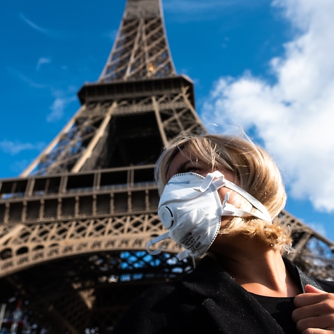 A woman with a face mask in front the Eiffel Tower in Paris.
