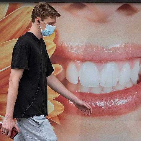 A young man wearing a face mask to curb the spread of COVID-19 walks past a photograph of a woman smiling outside a dental office, in Vancouver, on Monday, August 3, 2020. (Darryl Dyck/The Canadian Press via AP)