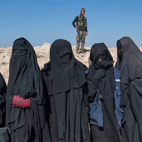  A fighter with the US-backed Syrian Democratic Forces (SDF) keeps watch near veiled women standing on a field after they fled from the Baghouz area in the eastern Syrian province of Deir Ezzor on February 12, 2019 during an operation to expel hundreds of