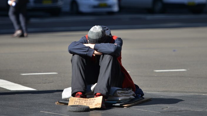 A homeless man sits on a street 