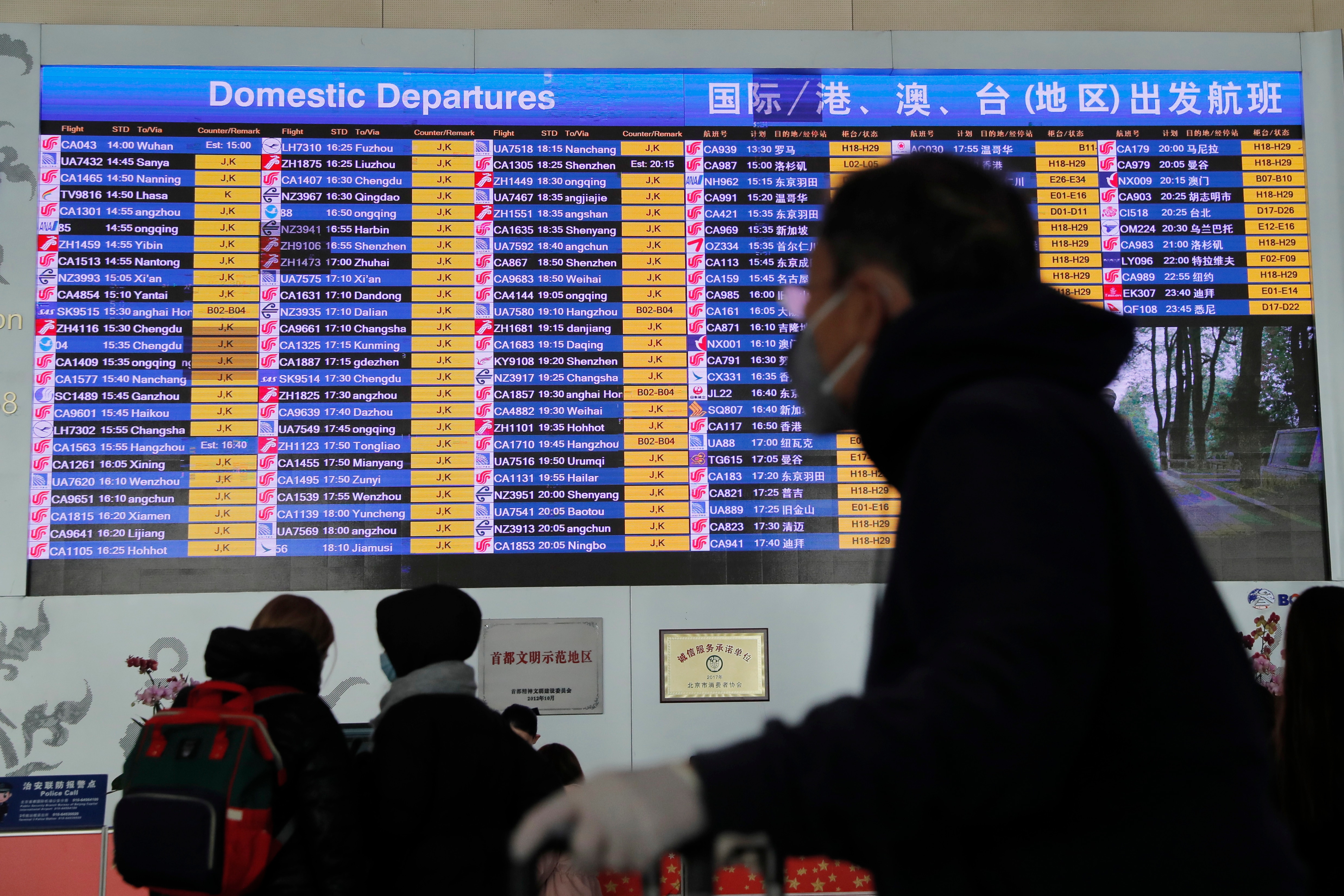 A passenger wears a mask passing by a departure information screen at Beijing Capital International Airport