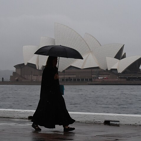 A pedestrian walks past the Sydney Opera House during wet weather in Sydney.