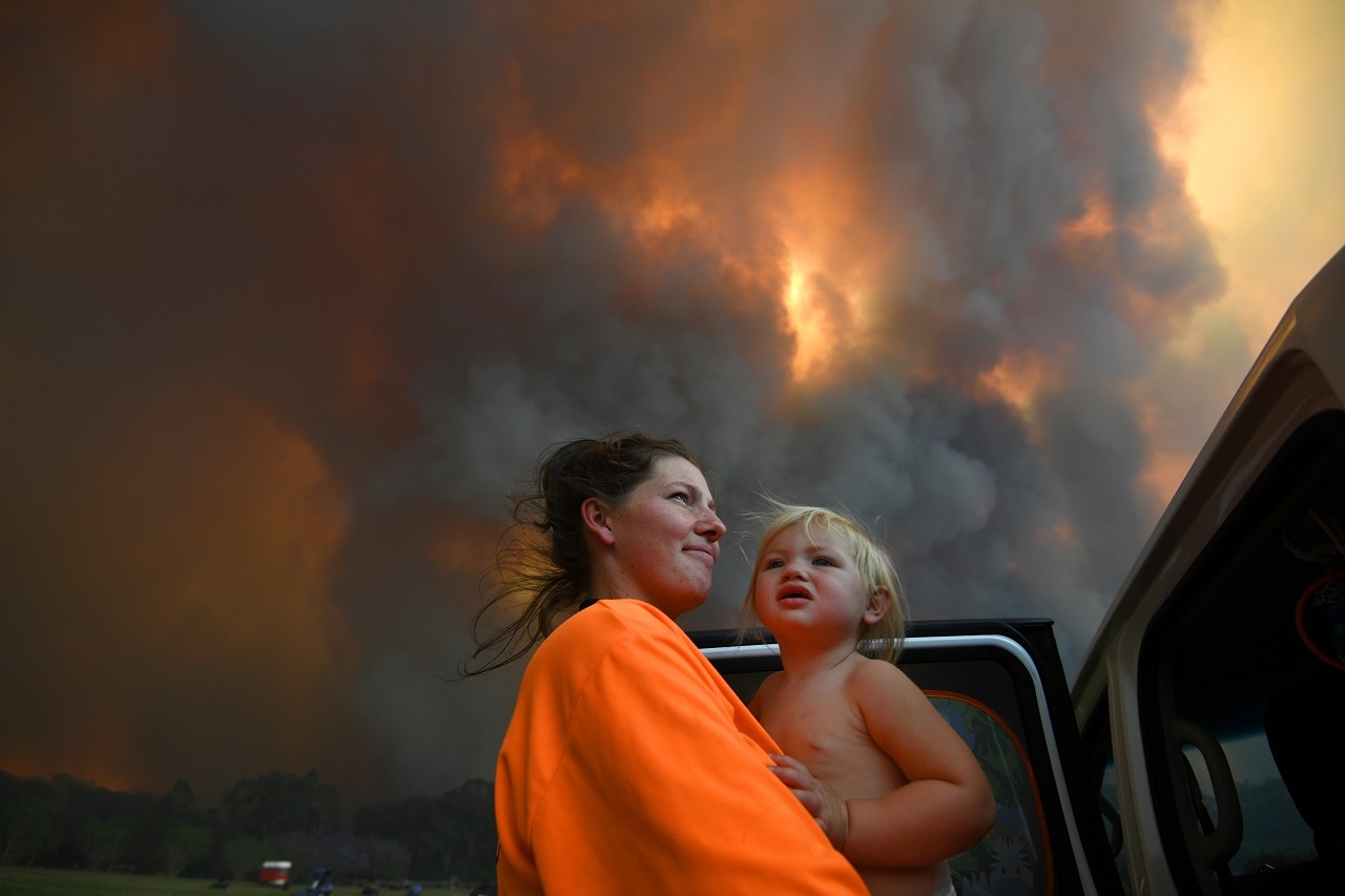 Sharnie Moren and her daughter Charlotte look on as thick smoke rises from bushfires near Nana Glen.