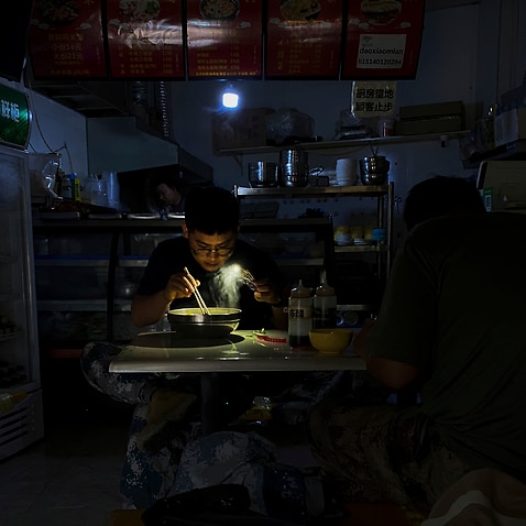 A man uses his smartphone flashlight to light up his bowl of noodles as he eats his breakfast at a restaurant during a blackout in Shenyang in northeastern China's Liaoning Province, Wednesday, Sept. 29, 2021. People ate breakfast by flashlight and shopke