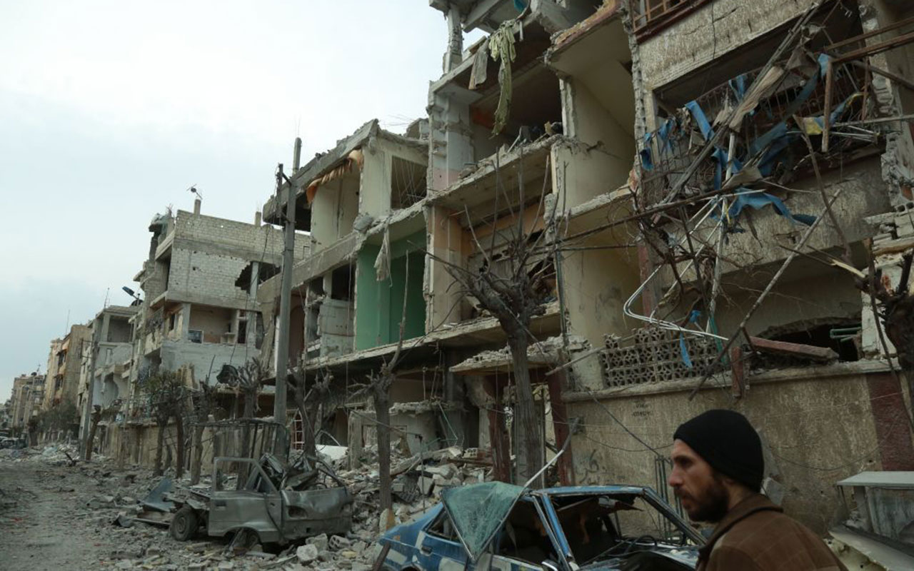 Picture taken on February 25, 2018, shows a Syrian man walking next to damaged buildings following regime air strikes.