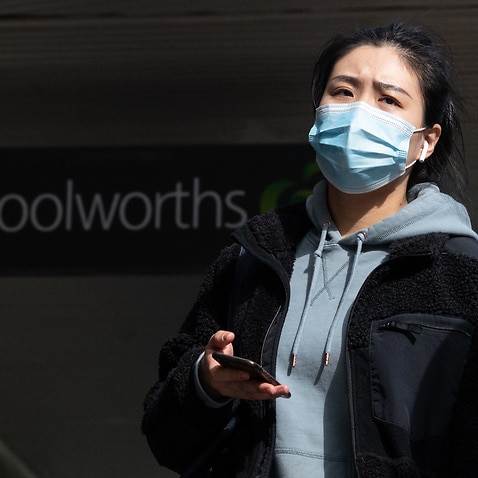 A person wearing a face mask in front of a Woolworths shop in Sydney.