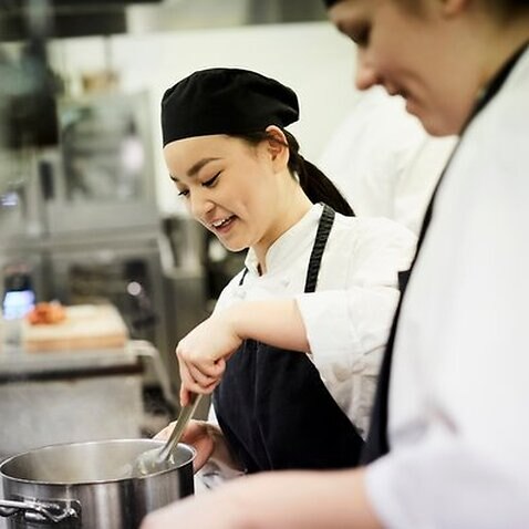 Female chef student with colleague cooking food in commercial kitchen