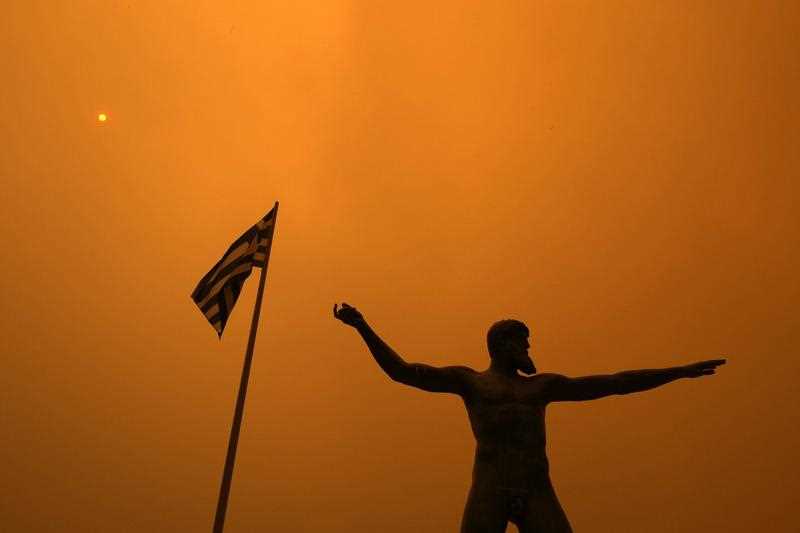 Smoke from a wildfire spreads over a statue at Pefki village on Evia Island north of Athens