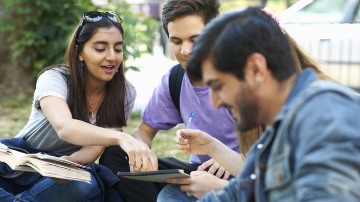 Male and female students sitting chatting and working on college campus