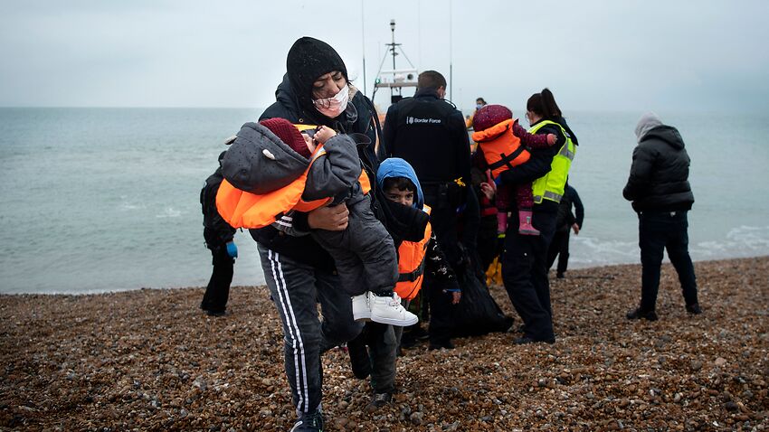 A migrant carries her children after being helped ashore from a RNLI (Royal National Lifeboat Institution) lifeboat at a beach in Dungeness, on the south-east coast of England, on November 24, 2021, after being rescued while crossing the English Channel.