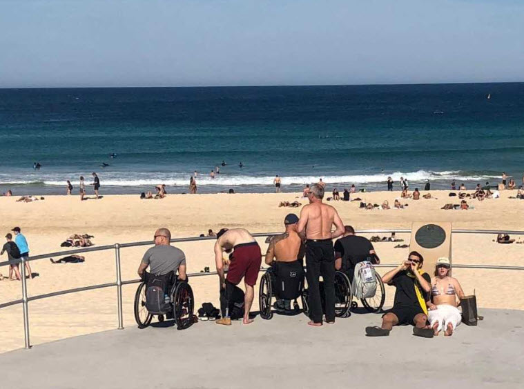 Wheelchair users unable to get onto the sand at Bondi Beach sit on the promenade.